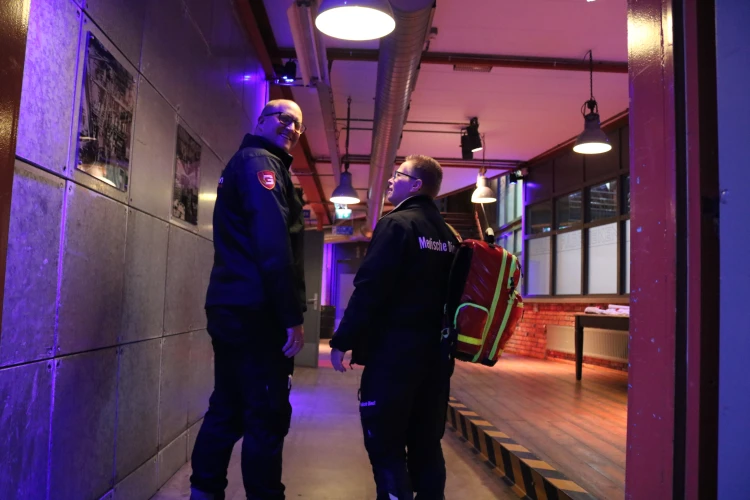 Twee medewerkers van Degrootbrandwachten die iets met elkaar bespreken terwijl er een van hun lachend in de camera kijkt